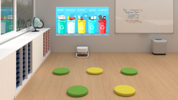 Une salle de classe avec un globe terrestre, un tableau blanc et des coussins de sol colorés. Un Netboard Portable affiche au mur des bacs de recyclage étiquetés pour le papier, les déchets organiques, le plastique, le verre et les déchets électroniques.