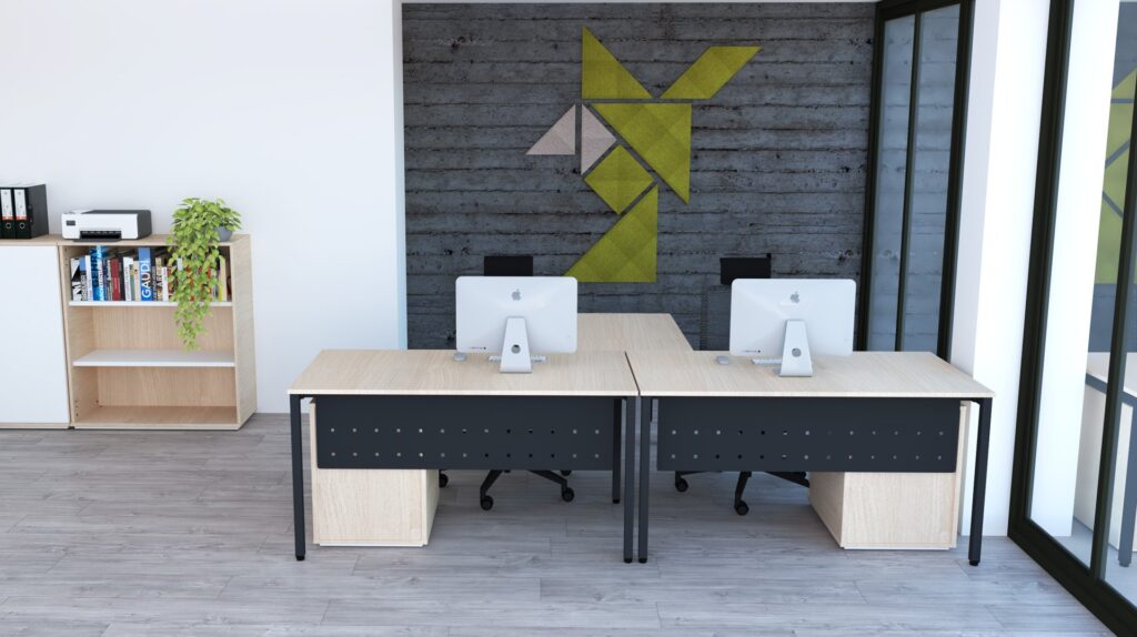 Bureau moderne composé de deux bureaux en bois, chacun équipé d'un iMac et d'une chaise de bureau, face à un mur gris avec des motifs géométriques verts et beiges. Une étagère avec des livres, des dossiers, une plante et une imprimante se trouve à gauche. De grandes baies vitrées se trouvent à droite.