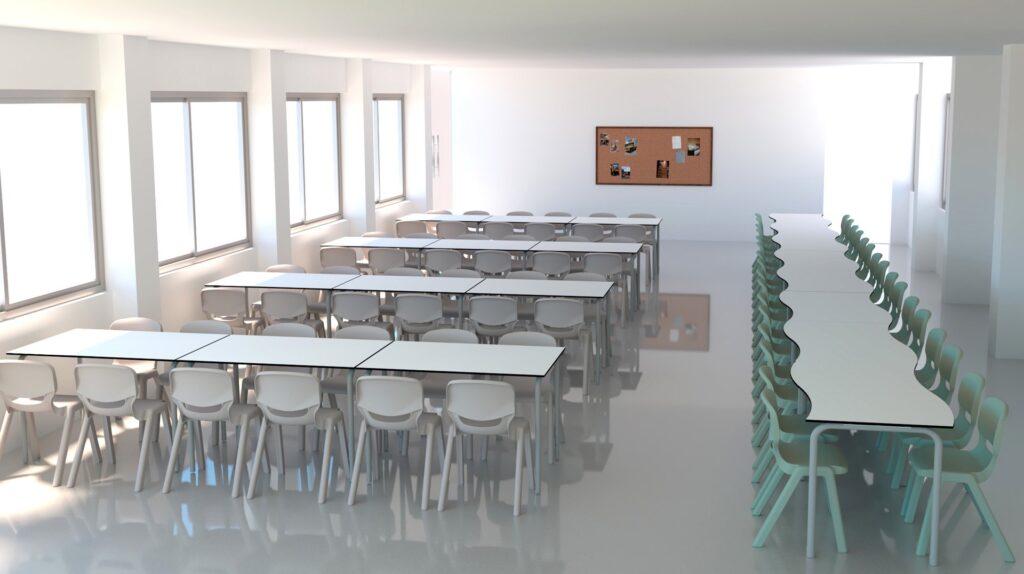 Une salle de classe moderne et lumineuse avec de grandes fenêtres, des rangées de bureaux et de chaises blanches sur la gauche, une longue table incurvée avec des chaises vertes sur la droite, et un tableau d'affichage en liège sur le mur du fond.