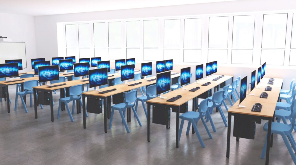 Un laboratoire informatique moderne avec des rangées de bureaux en bois, des chaises bleues et des ordinateurs de bureau sur chaque bureau. De grandes fenêtres bordent un mur, laissant entrer la lumière naturelle, et la salle semble propre et organisée.