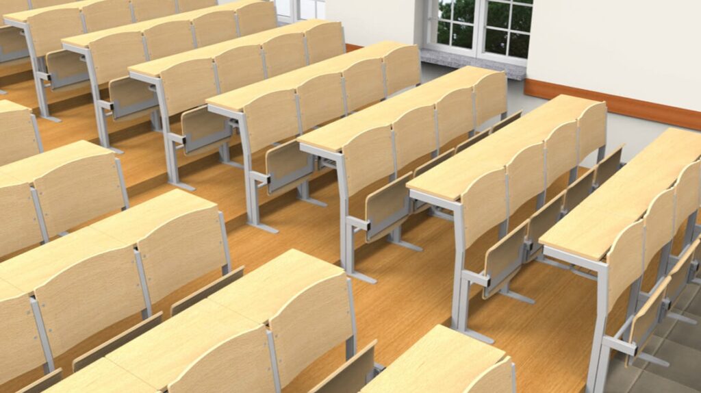 Des rangées de pupitres d'amphithéâtre en bois vides et de chaises à armature métallique sont disposées dans une salle de classe au sol en bois et aux grandes fenêtres, qui laissent entrer la lumière naturelle.