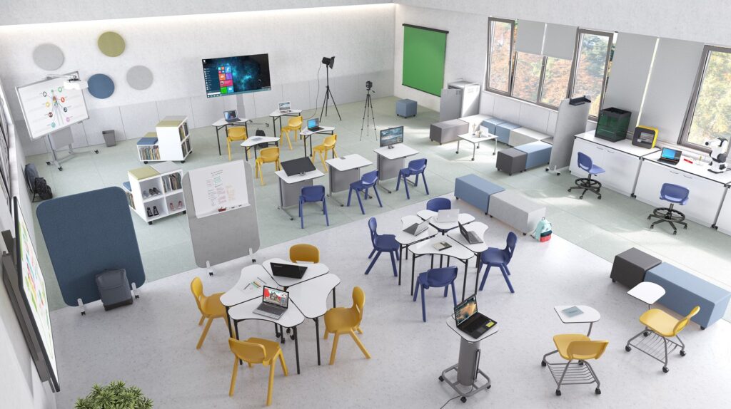 Une salle de classe moderne équipée de Nautilus Escolar muebles inteligentes, avec des chaises colorées, différentes tables, des ordinateurs, un écran vert, un trépied, un écran de télévision et de grandes fenêtres qui remplissent les espaces de travail organisés et l'espace ouvert avec de la lumière naturelle.