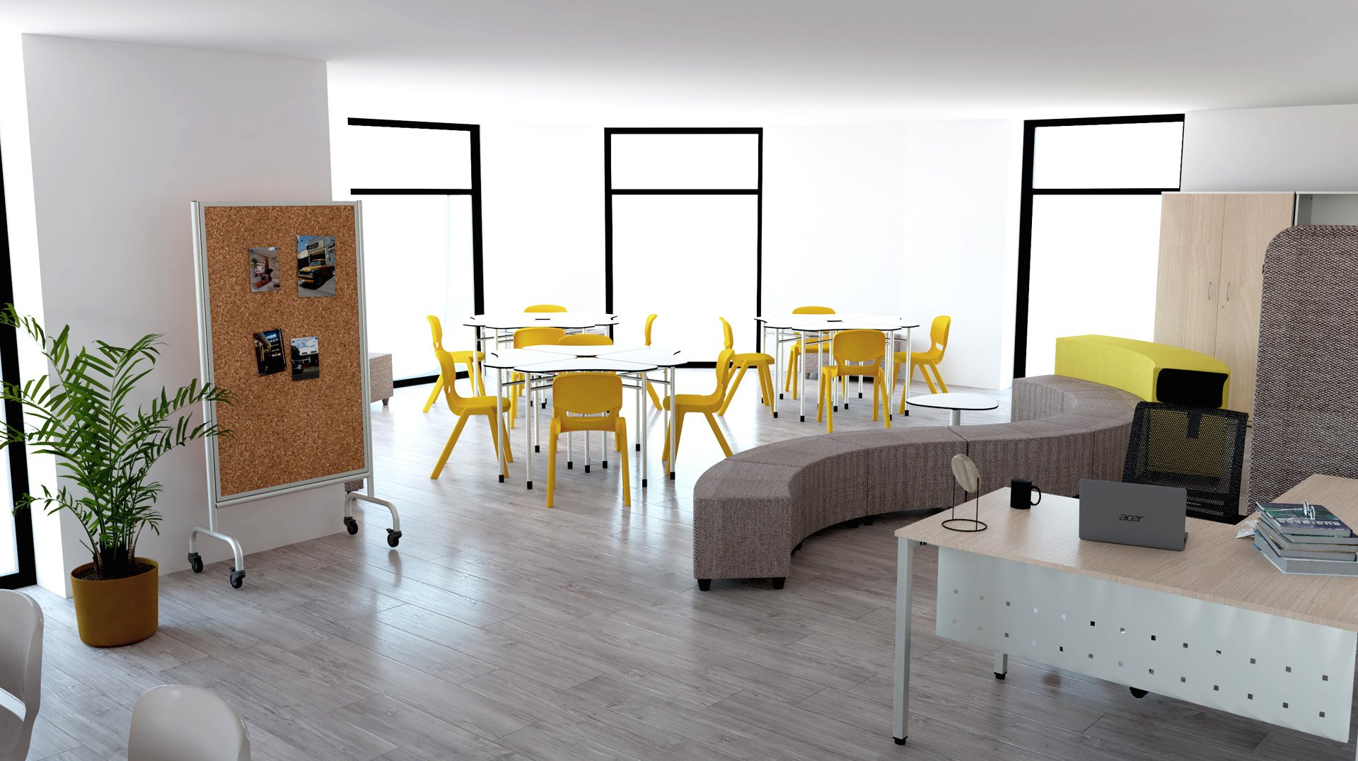Salle de classe moderne avec de grandes fenêtres, des chaises jaunes autour de tables rondes, un tableau de liège sur roulettes, un canapé gris incurvé et un bureau blanc avec un ordinateur portable et des livres - comme une mini-bibliothèque - ainsi qu'une plante verte sur un sol en bois clair.