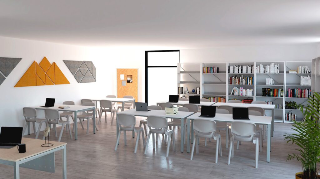 Une salle de classe moderne avec des murs, des tables et des chaises blancs. Des ordinateurs portables sont posés sur les tables, des étagères ressemblant à une bibliothèque miniature bordent le mur du fond et des œuvres d'art géométriques décorent l'un des murs. Une plante en pot trône dans cette pièce lumineuse et bien rangée.