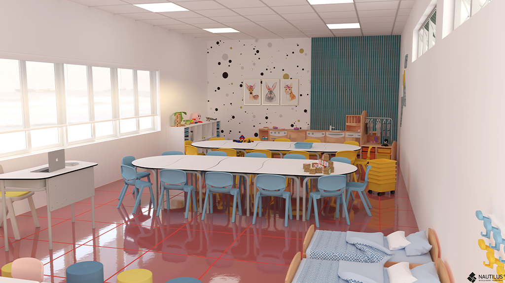Une salle de classe moderne et lumineuse avec des chaises colorées autour de tables blanches, des jouets éducatifs, des étagères et des œuvres d'art sur le mur du fond. De grandes fenêtres bordent un côté, et un petit lit avec des draps bleus se trouve dans le coin.