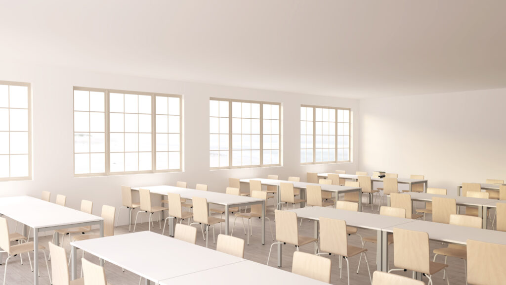 Une salle de classe lumineuse et spacieuse avec de grandes fenêtres, des rangées de chaises en bois vides et des tables blanches bien rangées, créant un environnement ordonné et propre qui rappelle une bibliothèque tranquille.