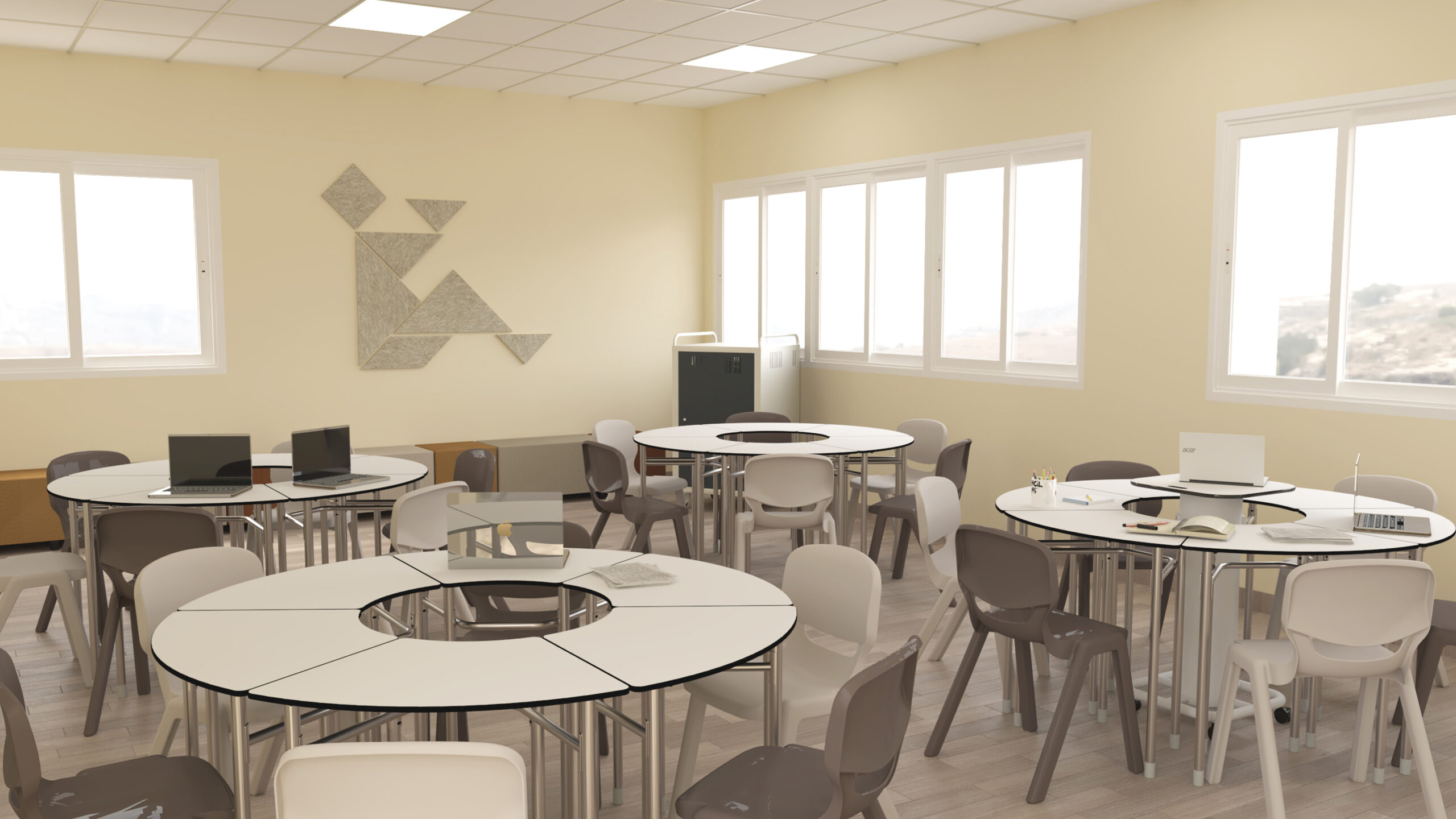 Une salle de classe Aula Mentor lumineuse au CEPA avec des tables rondes et des chaises grises, des ordinateurs portables et des livres sur les tables, de grandes fenêtres laissant entrer la lumière naturelle, et un art mural géométrique sur un mur de couleur crème.
