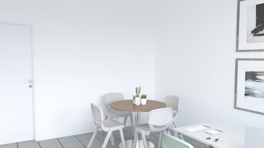 Une salle des enseignants minimaliste comprend une table ronde avec quatre chaises grises, deux petites plantes en pot sur la table, un bureau blanc avec des papiers et des stylos, et des œuvres d'art abstraites sur les murs blancs.