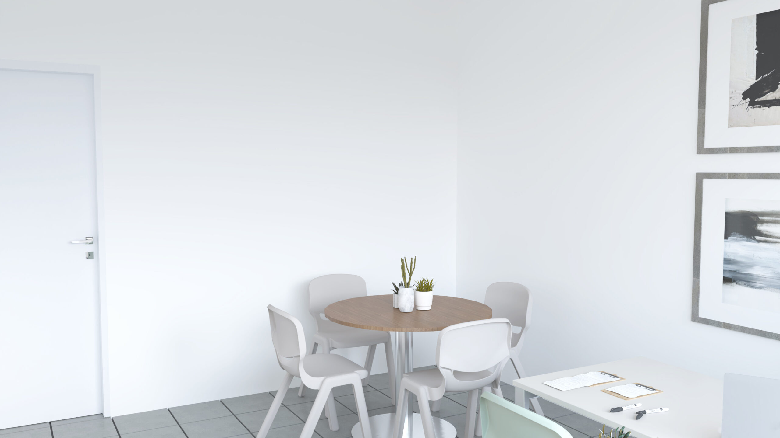 Une salle des enseignants minimaliste comprend une table ronde avec quatre chaises grises, deux petites plantes en pot sur la table, un bureau blanc avec des papiers et des stylos, et des œuvres d'art abstraites sur les murs blancs.