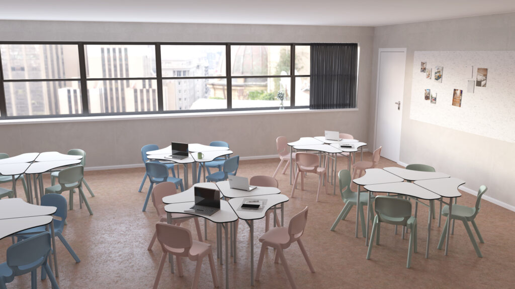 Une salle de classe moderne de l'École numérique avec des tables hexagonales, des chaises aux couleurs pastel et des ordinateurs portables ouverts. De grandes fenêtres offrent une vue sur la ville et un tableau d'affichage avec des photos est accroché au mur près d'une porte fermée.