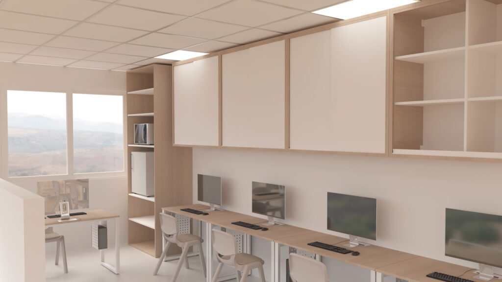Une salle informatique moderne avec des bureaux, des chaises, plusieurs ordinateurs de bureau et des armoires murales ; adjacente à la Salle des enseignants, la salle est dotée de grandes fenêtres pour la lumière naturelle et d'un design épuré et minimaliste dans des couleurs neutres.